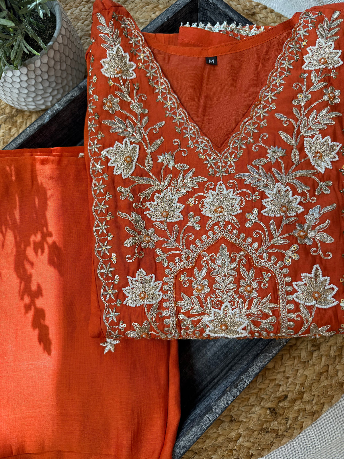 Orange traditional outfit with intricate white Gold embroidery on a Muslin Cotton surface.